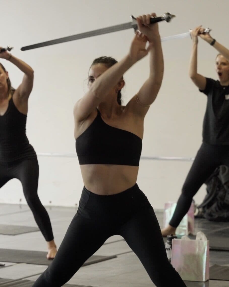 Three dancers moving in unison with their swords raised overhead
