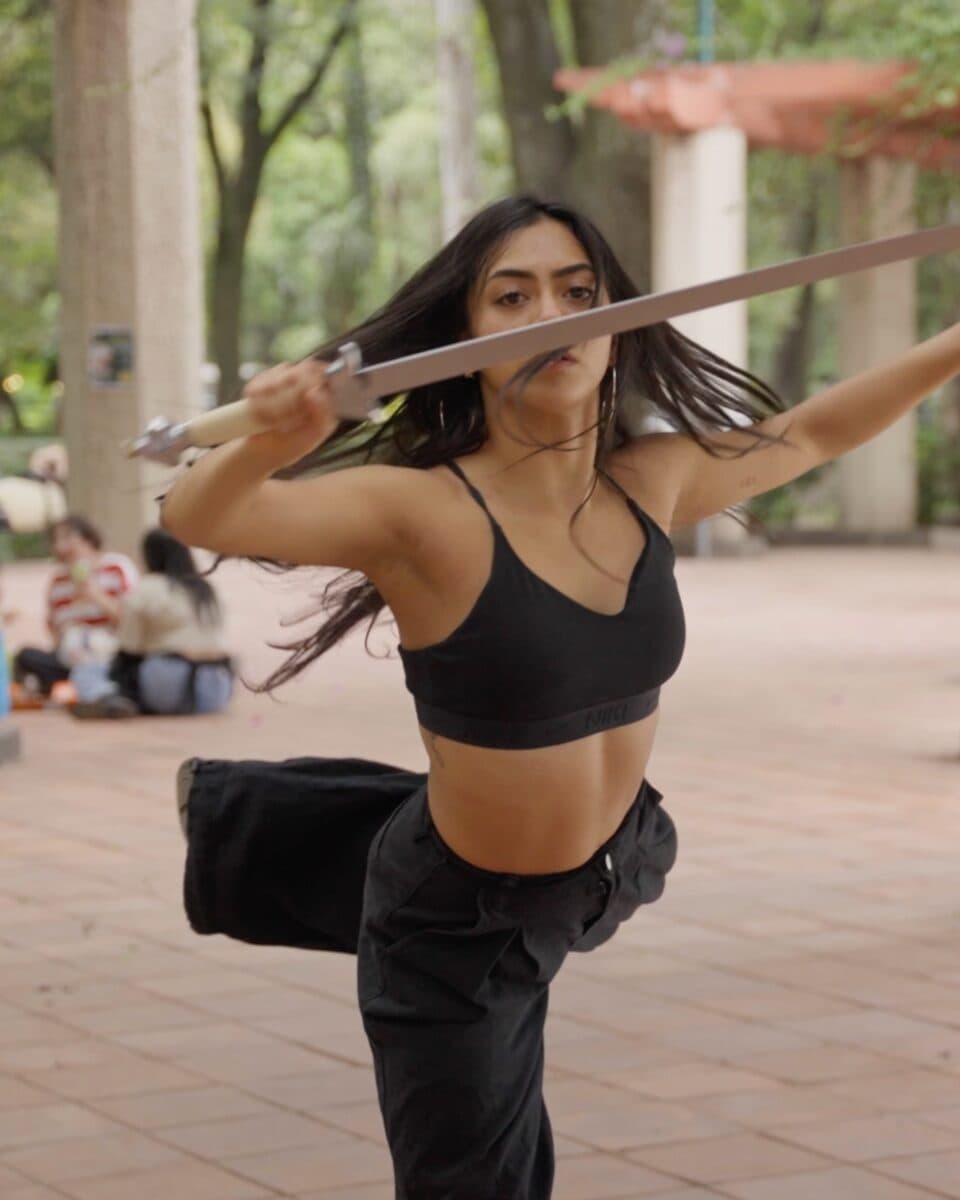 A dancer moving with a sword beneath a park pergola in Mexico City