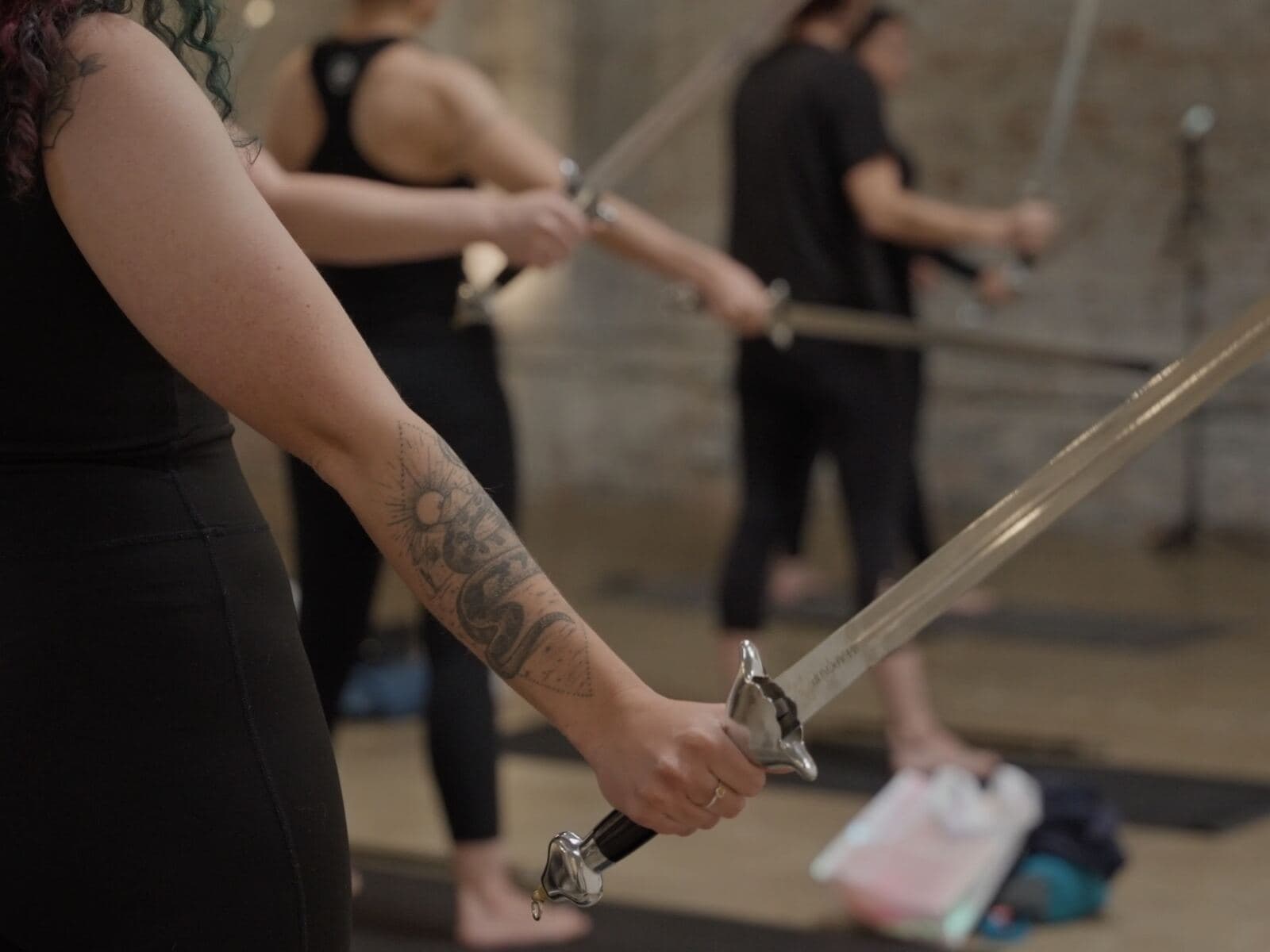 Close-up of a member’s tattooed arm holding a sword during a WeaponUp class